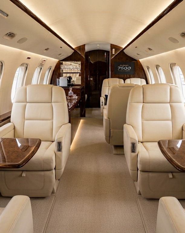 Private aircraft cabin with cream leather interior, oval windows and wood trim.